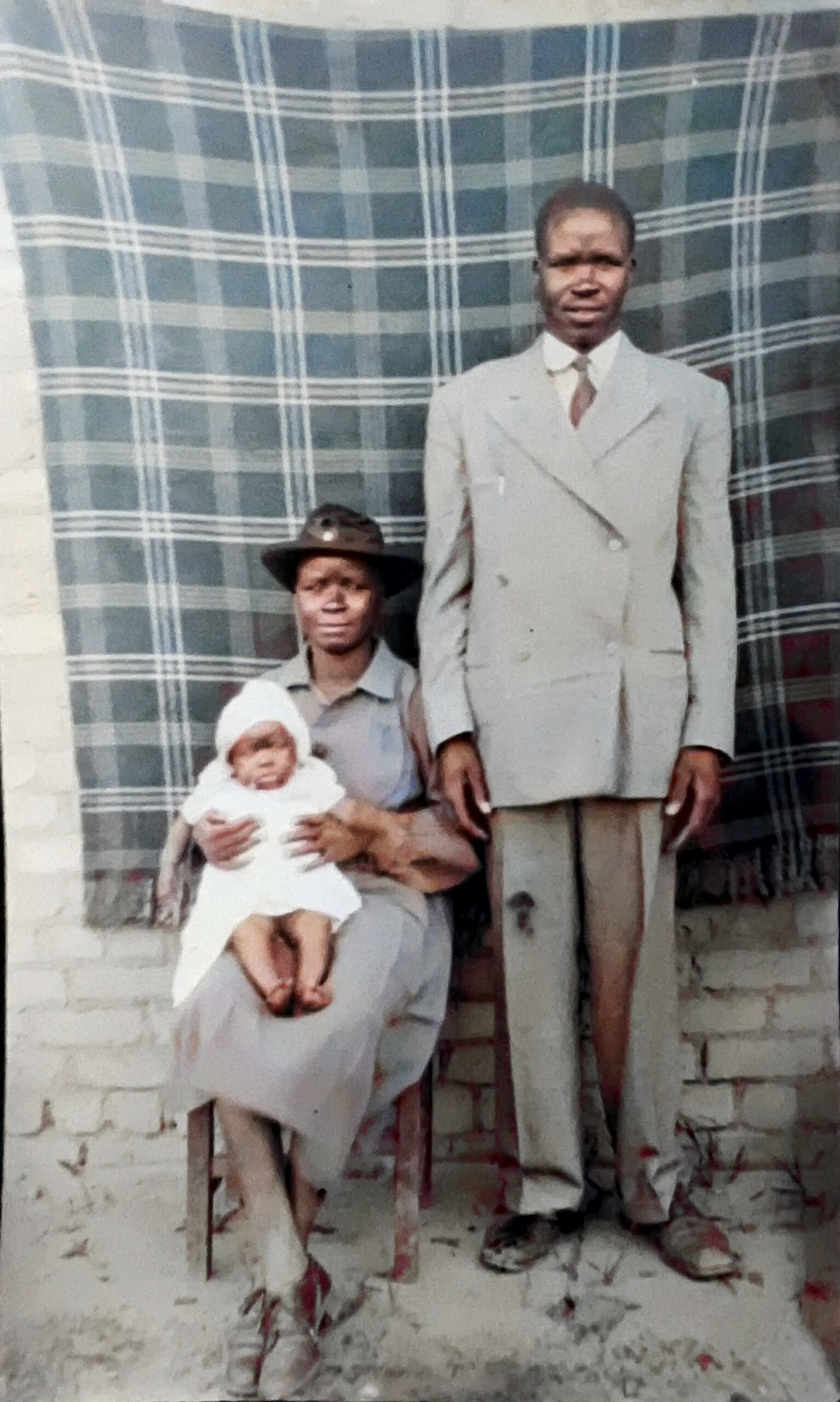 A picture of Black couple posing for a portrait. The woman holds a baby on her lap